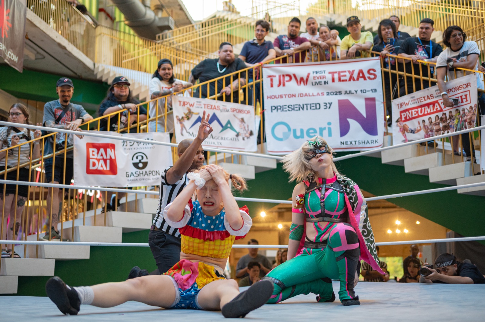 Two Tokyo Joshi Pro Wrestling performers pose in the ring at POST Houston beneath a banner reading 'TJPW First Ever Live in Texas — presented by Queri and NextShark,' with fans watching from the venue's terraced steps